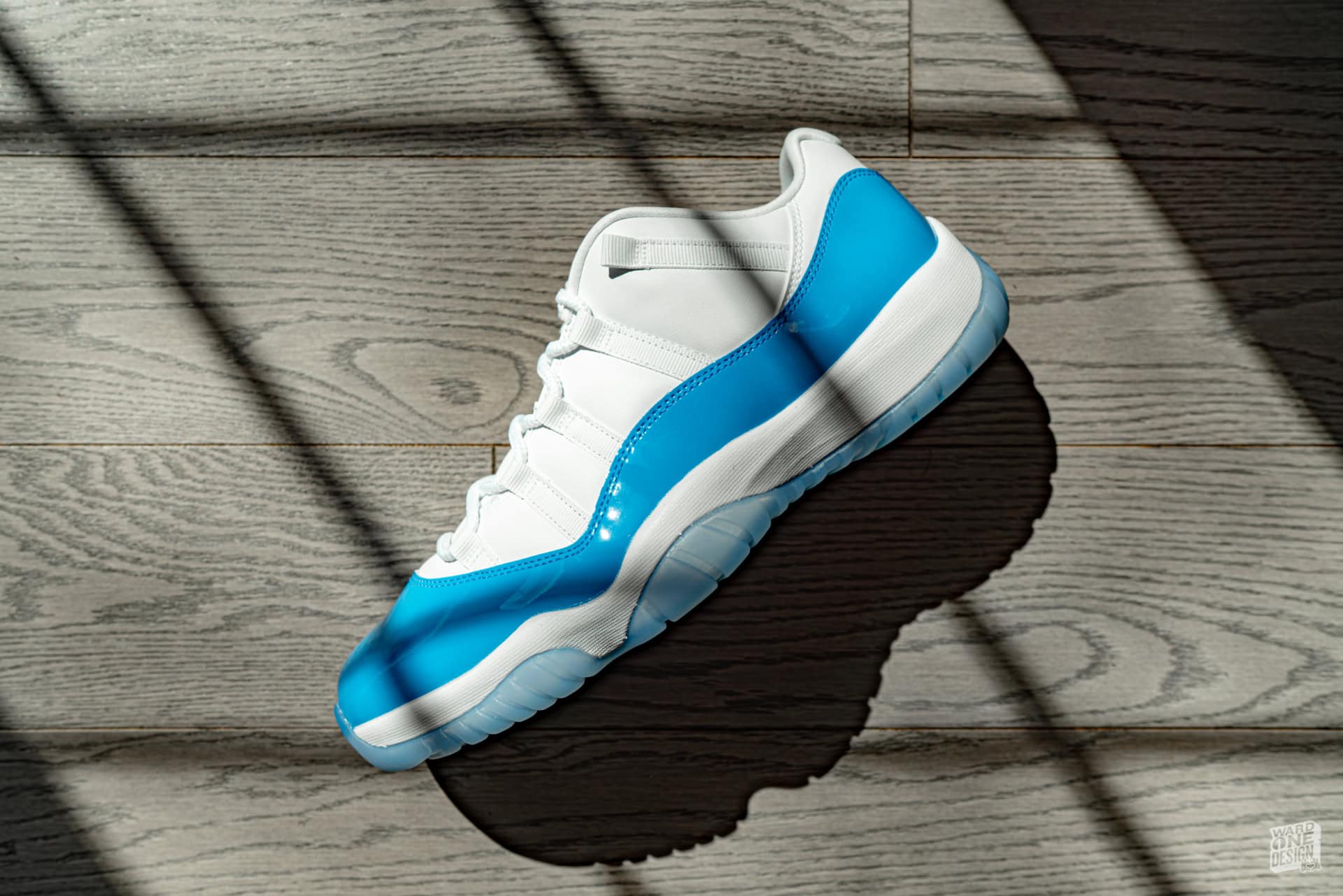 Close-up of Air Jordan 11 Retro sneakers in white and blue, placed on a wooden floor with shadows highlighting their design. Perfect for sneaker enthusiasts and collectors.