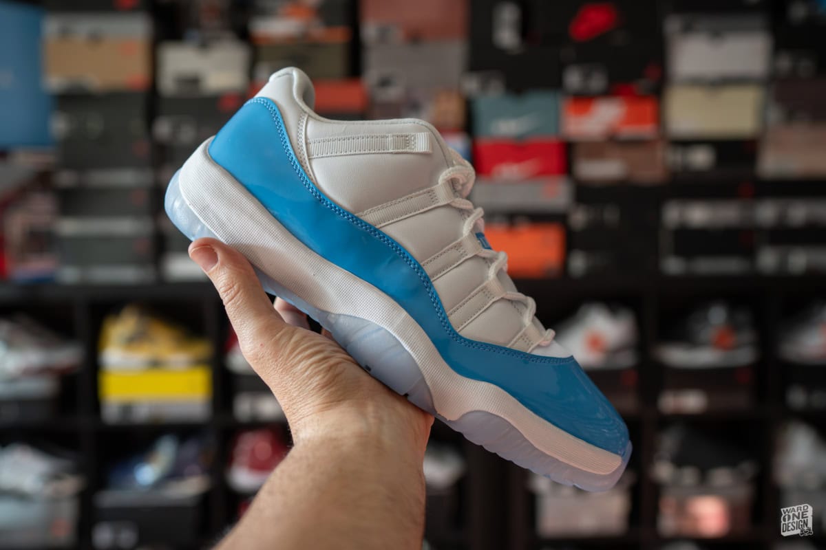 Close-up of Air Jordan 11 Retro Low UNC sneaker held in hand, showcasing the iconic white and University Blue colorway, perfect for sneaker enthusiasts and collectors.