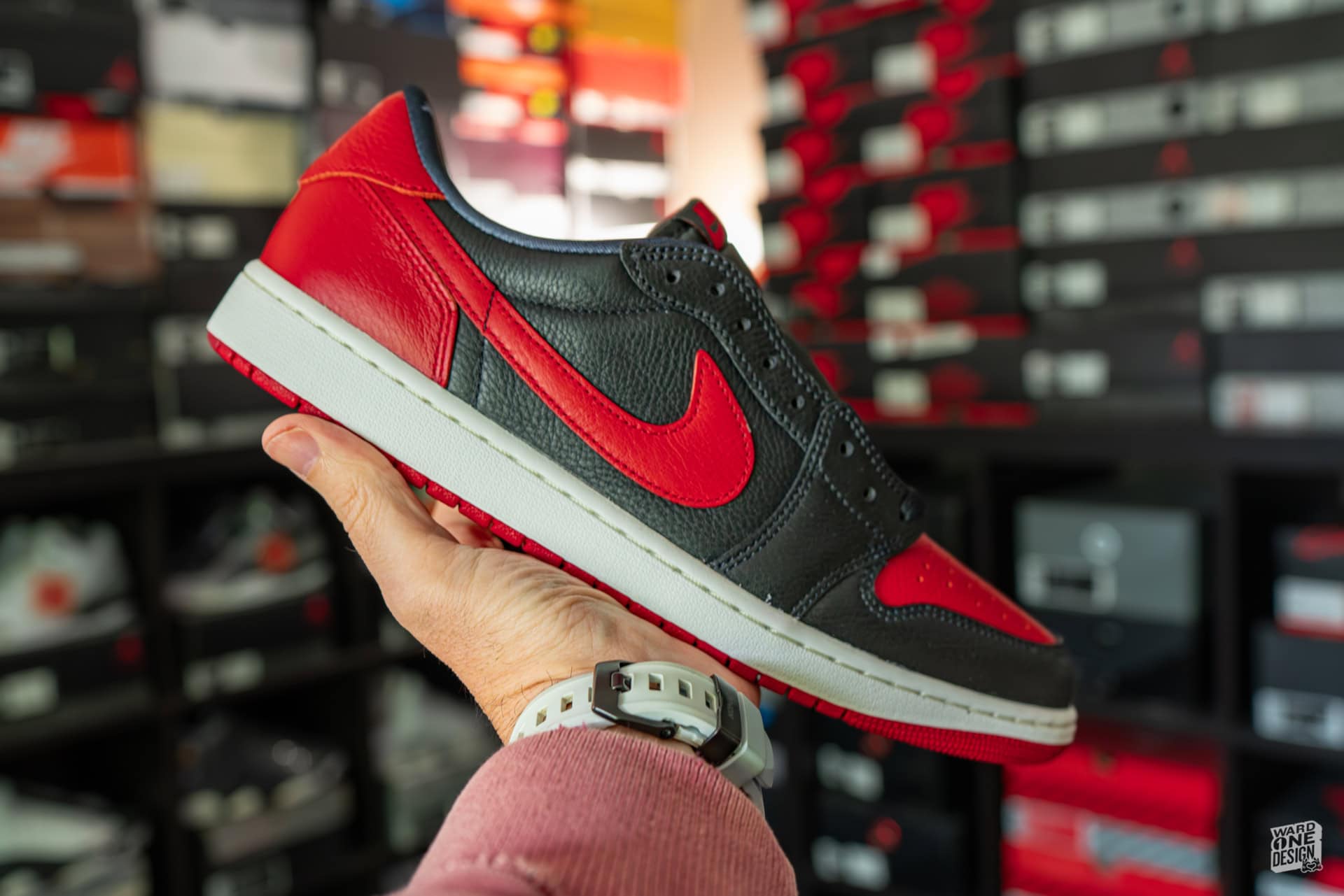 Close-up of Air Jordan 1 Retro Low OG "Banned" sneaker in black and red, held in hand with a shoe store background. Perfect for sneaker enthusiasts and collectors.