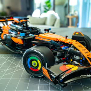 Detailed Lego model of the McLaren MCL39 F1 car in orange and black, displayed on a worktable with a modern living room background.