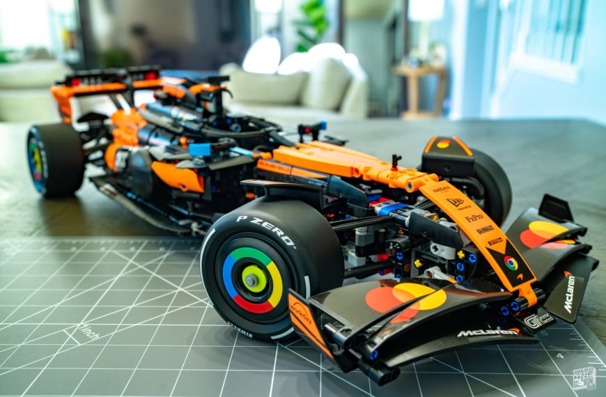 Detailed Lego model of the McLaren MCL39 F1 car in orange and black, displayed on a worktable with a modern living room background.
