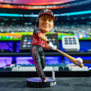Close-up of a Colson Montgomery White Sox bobblehead figure with a baseball bat, set against a colorful sports event background.