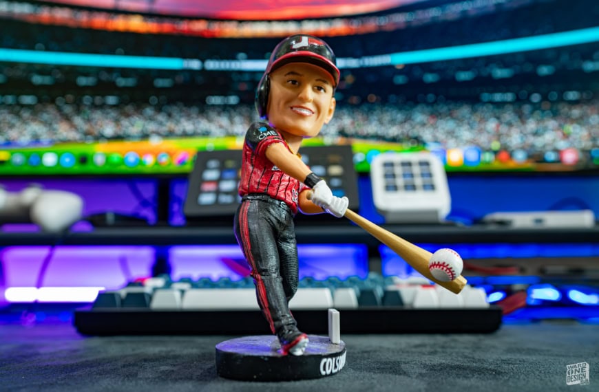 Close-up of a Colson Montgomery White Sox bobblehead figure with a baseball bat, set against a colorful sports event background.