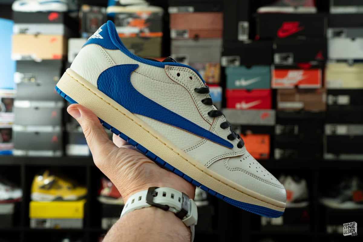 Close-up of a hand holding a white and blue Nike sneaker in a sneaker store with shelves of shoes in the background.
