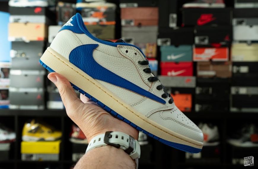 Close-up of a hand holding a white and blue Nike sneaker in a sneaker store with shelves of shoes in the background.
