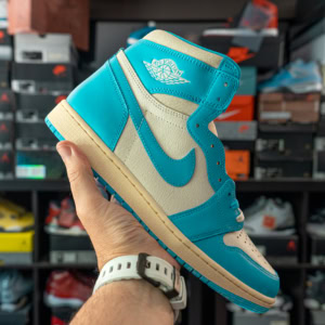Close-up of Air Jordan 1 High OG UNC Reimagined sneakers held in hand, showcasing the vibrant blue and cream colorway with iconic Nike swoosh, in a sneaker store setting.