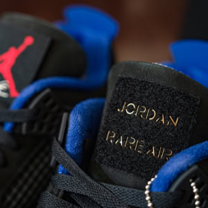 Close-up of Air Jordan 4 Rare Air sneakers featuring black and blue colorway with gold "Rare Air" branding on the tongue. Perfect for sneaker collectors and Jordan enthusiasts.