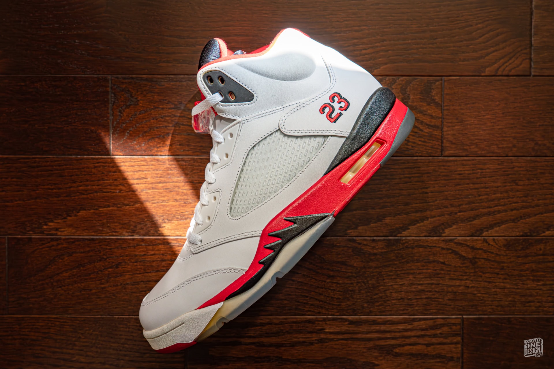 Classic Air Jordan 5 Fire Red sneaker with white, red, and black accents, featuring the number 23 on the side, displayed on a wooden floor. Perfect for sneaker enthusiasts and collectors.