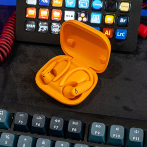 Close-up of yellow Beats Powerbeats Pro 2 wireless earbuds in charging case on desk with keyboard and editing equipment.