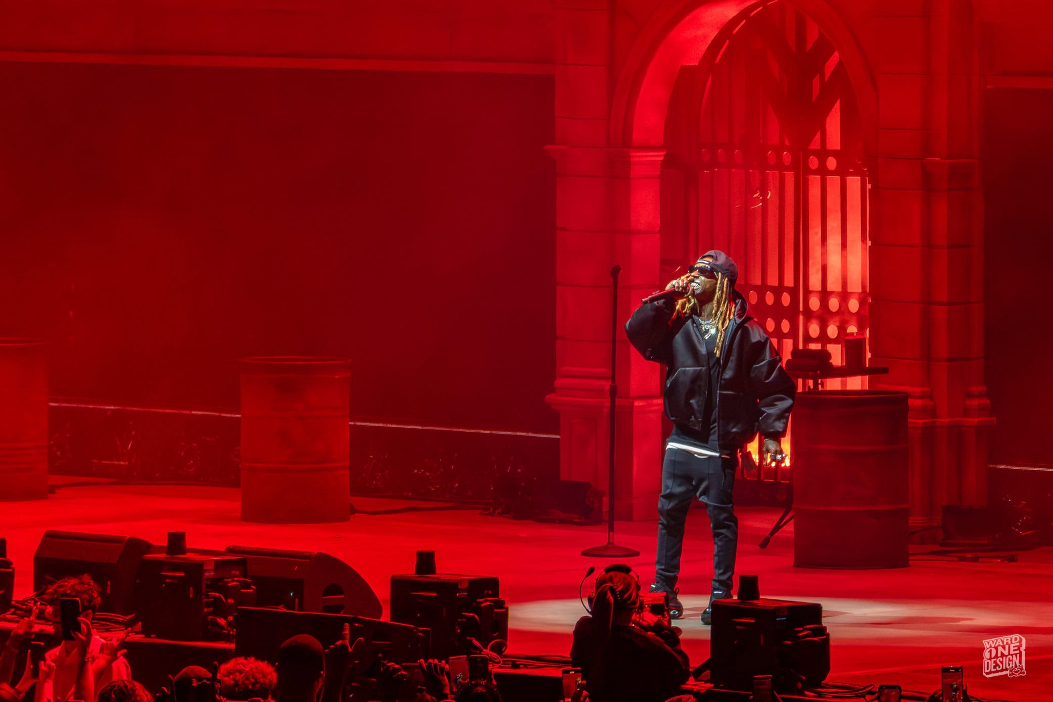 Lil Wayne on stage during Tha Carter VI Tour, illuminated by red lighting, performing passionately with a microphone in hand at a concert venue.