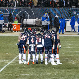 Chicago Bears and Los Angeles Rams players huddle during the NFC Division Championship football game on a rainy day.