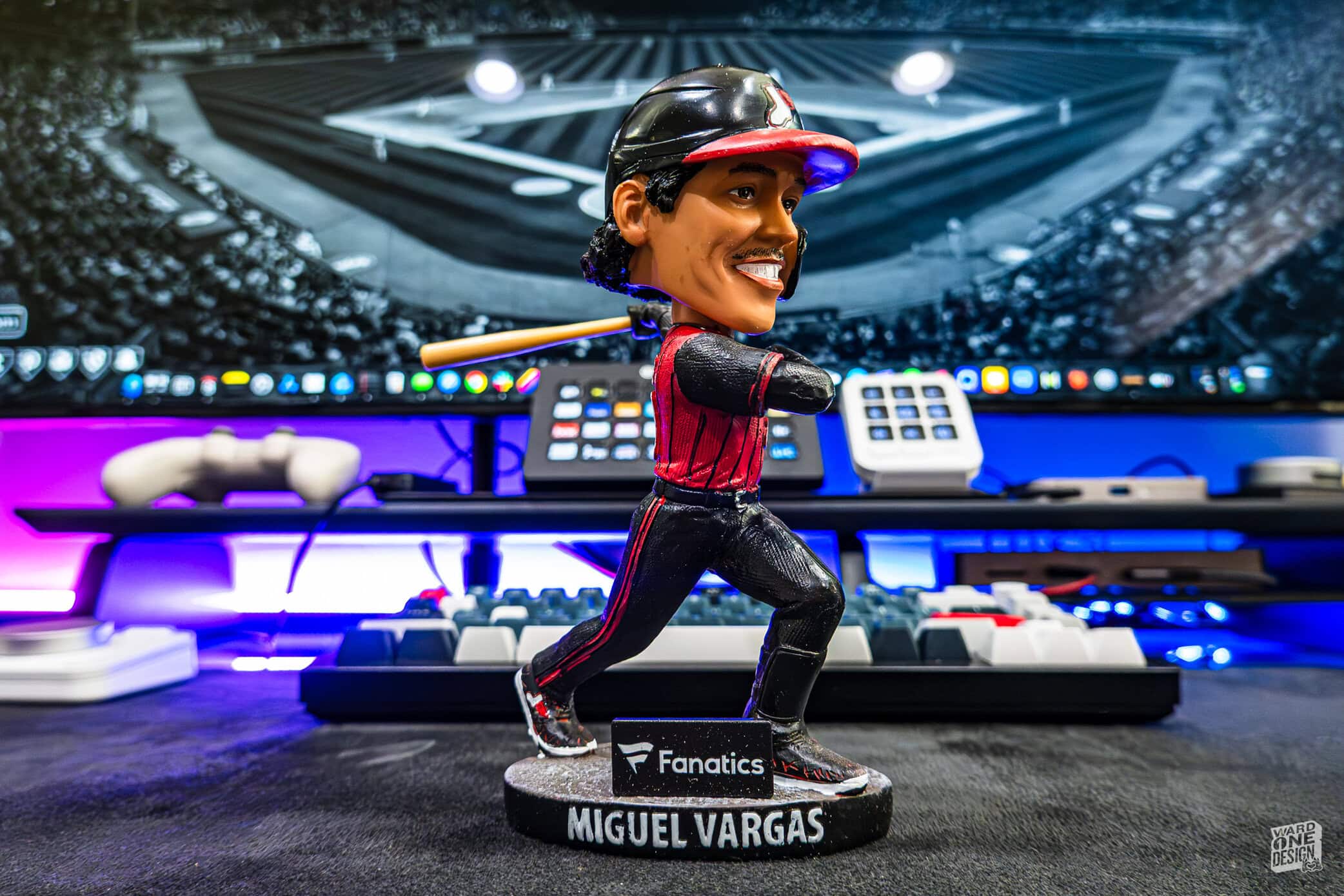 A detailed figurine of Miguel Vargas, a professional esports player, displayed at a gaming event with vibrant lighting and gaming equipment in the background.