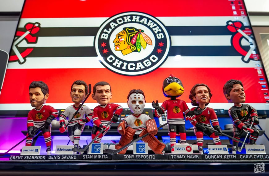 Collection of Chicago Blackhawks themed bobblehead figures featuring team players and mascot, displayed on a shelf with team logo in the background.