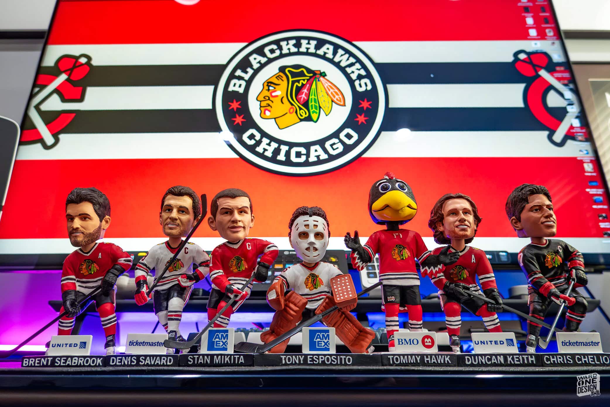 Collection of Chicago Blackhawks themed bobblehead figures featuring team players and mascot, displayed on a shelf with team logo in the background.