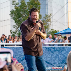 Male singer passionately performing with microphone at outdoor concert, crowd enjoying the live music, urban setting with modern buildings in the background.