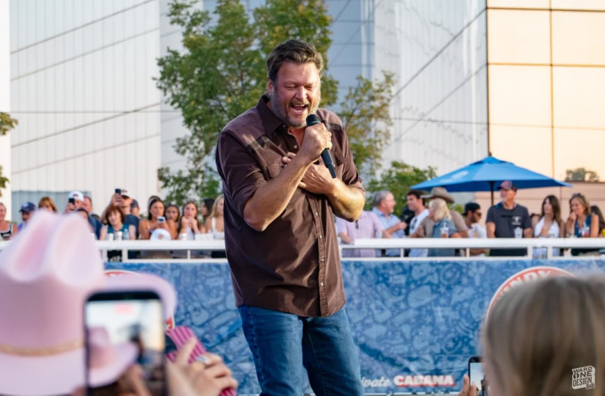 Male singer passionately performing with microphone at outdoor concert, crowd enjoying the live music, urban setting with modern buildings in the background.