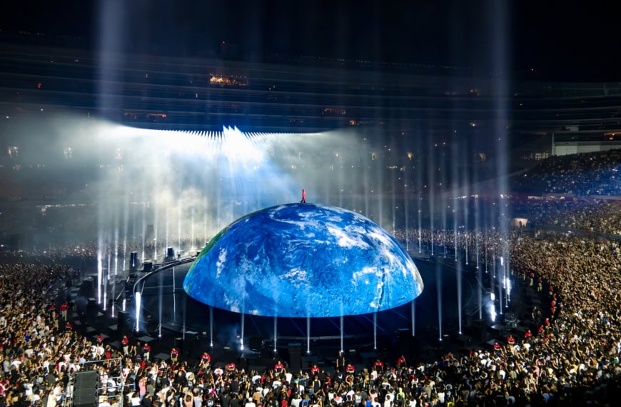 Large globe projection at a concert with water fountains and a massive crowd, emphasizing environmental awareness and global unity.